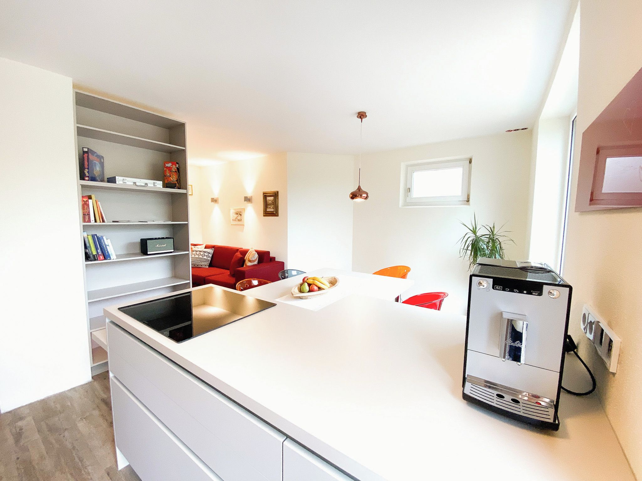 A modern kitchen with a white countertop, a red sofa, and a small dining table.