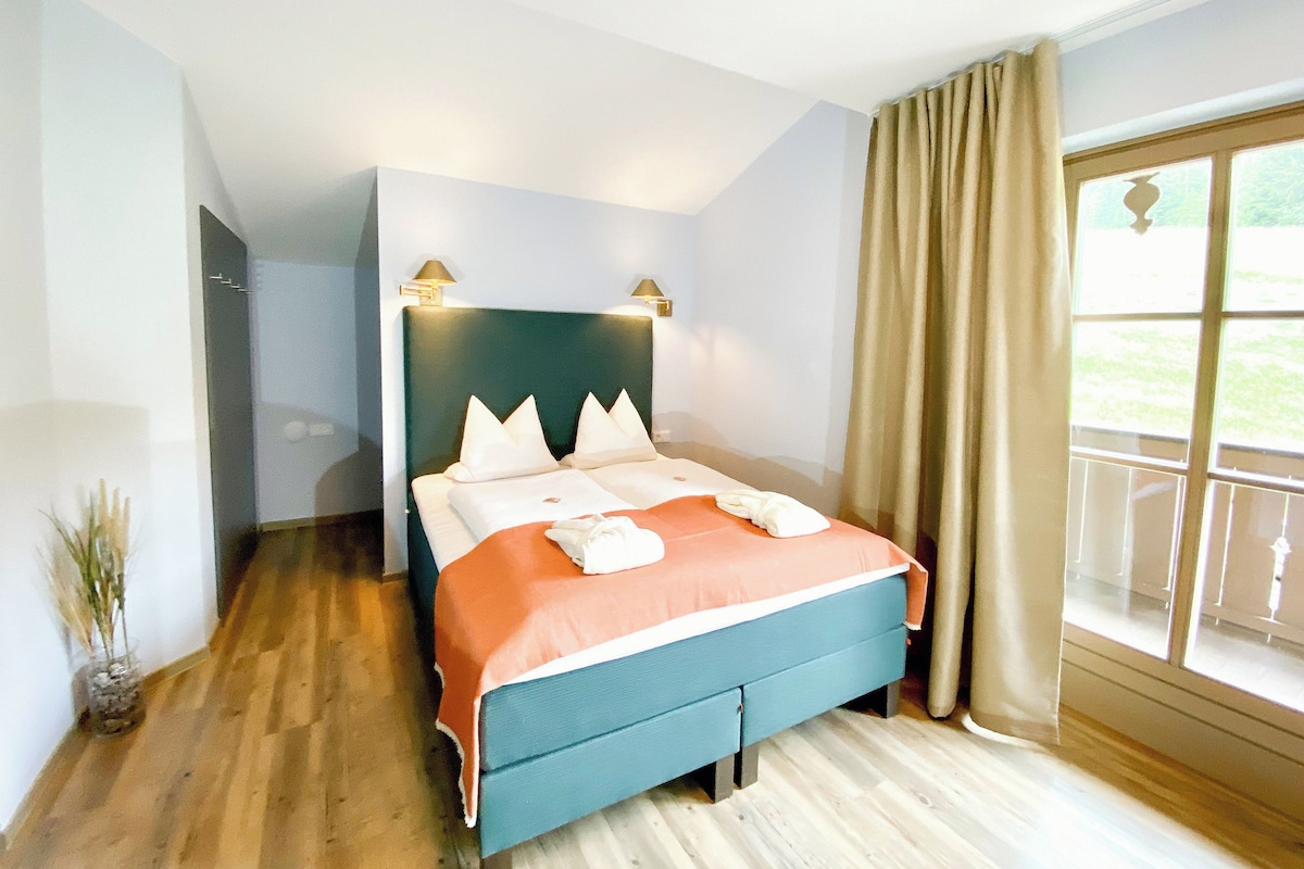 Ein Hotelzimmer mit einem Bett, einem Fenster mit Vorhängen, einer Zimmerpflanze und Holzboden.
