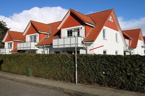 A row of modern houses with red-tiled roofs and white walls, featuring balconies and a hedge in the foreground. - Holiday apartment with 2 bedrooms (Cuxhaven)