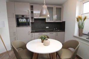A modern kitchen with a built-in oven, a round dining table with chairs, and a pendant light. - Holiday apartment with 2 bedrooms (Cuxhaven)