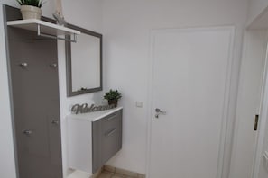 A bathroom with a white vanity, a mirror, a potted plant, and a door. - Holiday apartment with 2 bedrooms (Cuxhaven)