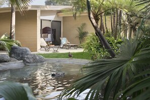 Ein Pool mit einer Ente, umgeben von Palmen und einem Gebäude mit einer Schiebetür.