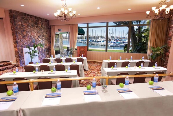 Ein Konferenzraum mit für eine Besprechung gedeckten Tischen, einer Steinwand, Blick auf Boote durch große Fenster und einer Chandelüster.