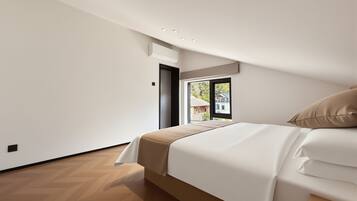 A bedroom with a bed, a window with a view, and a herringbone-patterned floor.