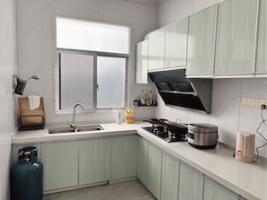 A modern kitchen with a built-in stove, a gas cylinder, and a window with blinds. - Hedui Scenic Homestay - Zhangjiajie (Zhangjiajie)