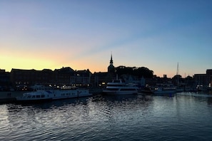 A waterfront cityscape at dusk with boats docked, a prominent tower, and buildings lining the shore. - Holiday apartment with 1 bedroom (Olpenitz)