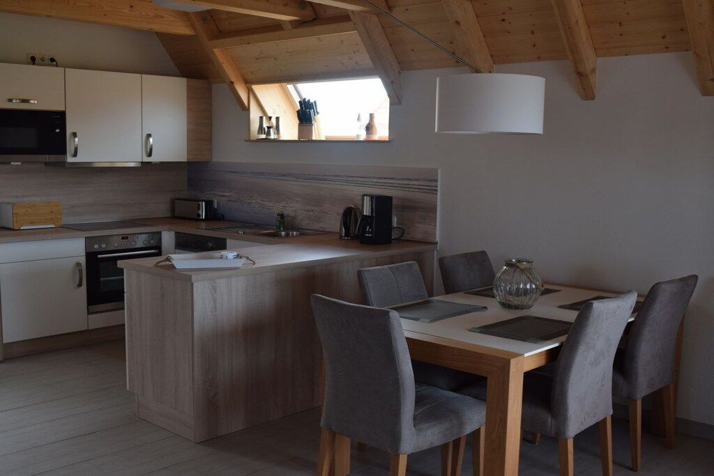 Una cocina moderna con armarios de madera, una isla central y un comedor con sillas grises.