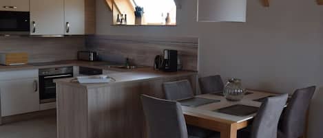 A modern kitchen with wooden cabinets, a central island, and a dining area with grey chairs.