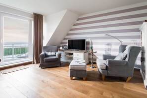 A modern living room with a TV, two armchairs, a small table, and a desk. - Holiday apartment in Juist with swimming pool (Juist)
