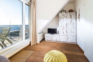 A room with a large window, a television, a white cabinet, and a wooden floor. - Holiday apartment in Juist with swimming pool (Juist)