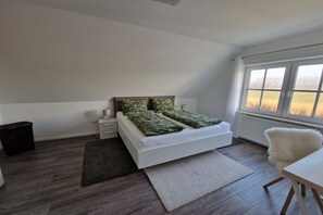 A bedroom with a bed, bedside tables, a window, and a view of the outdoors. - Holiday apartment with 1 bedroom (Dornum)