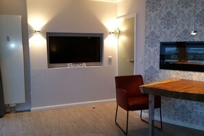 Ein modernes Wohnzimmer mit einem an der Wand befestigten Flachbildfernseher, einem roten Sessel und einem Holzessttisch.