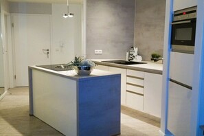 A modern kitchen with a central island, a built-in oven, and a sink. - Beach sea view apartment (Borkum)