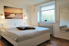 Ein Schlafzimmer mit einem Bett, einem Fenster mit Jalousien, einem Heizkörper und einem Wandbild.