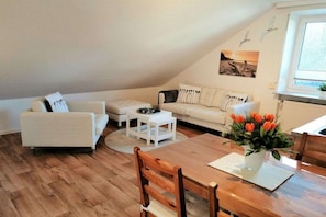 Ein Wohnzimmer mit einer Couch, einem Esstisch und einer Blumenvase.