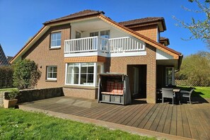 A two-story house with a balcony, a deck, and a patio area. - Beach holiday home at Tabakshof (Sierksdorf)