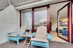Ein Balkon mit zwei Stühlen und einem Tisch, ein großes Fenster und Blick ins Innere.