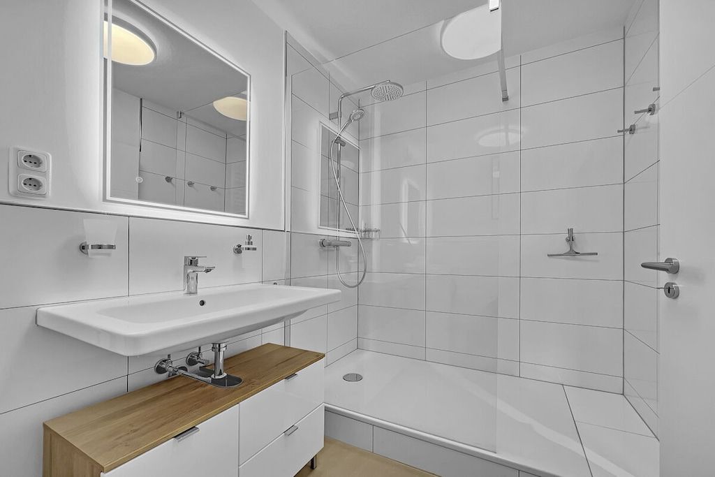 Une salle de bain moderne avec un lavabo blanc, un miroir et une douche.