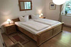 Ein Doppelbett mit Holz-Kopf- und Fußteil, zwei Nachttische mit Lampen, ein Spiegel an der Wand und ein Fenster mit Vorhängen.