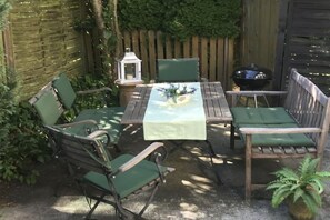 Eine Terrass mit Tisch, Stühlen, einer Laterne und einem Grill.