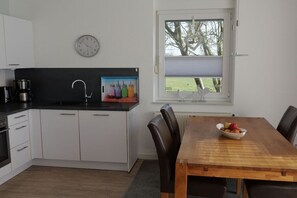 A modern kitchen with white cabinets, a black countertop, a coffee maker, and a clock on the wall. - Borkum sun apartment (Borkum)
