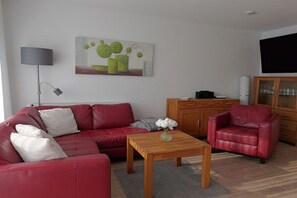 A living room with a red sofa, a wooden coffee table, a red armchair, a cabinet, and a painting on the wall. - Borkum sun apartment (Borkum)