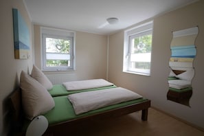 Ein Schlafzimmer mit zwei Betten, einem Heizkörper und einem Fenster mit Blick auf Bäume.