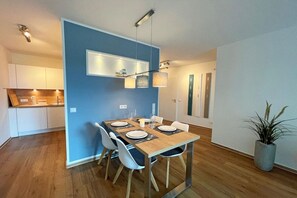 A modern dining area with a wooden table set for four, white chairs, and pendant lighting. - Holiday apartment with 2 bedrooms (Kappeln)