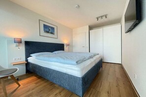 A modern bedroom with a bed, bedside lamps, a chair, and a wardrobe. - Holiday apartment with 2 bedrooms (Kappeln)