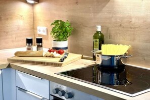 A kitchen with a stove, a cutting board with vegetables, a pot of pasta, a bottle of olive oil, and a potted plant. - Holiday apartment with 2 bedrooms (Kappeln)
