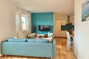 A living room with a sofa, a television, and a kitchen area in the background. - Holiday apartment with 2 bedrooms (Sierksdorf)