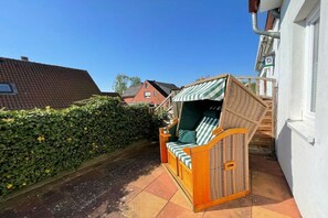 A wicker outdoor seating area with cushions, adjacent to a white building with a tiled roof. - Holiday apartment with 2 bedrooms (Sierksdorf)