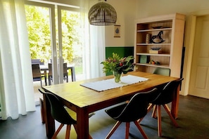 A dining area with a wooden table, black chairs, a vase with flowers, and a bookshelf with decorative items. - Country House Moor and Sea (Ostgroßefehn)