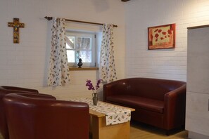 A room with a wooden table, two leather chairs, a window with curtains, a vase with flowers, and a wall-mounted cross. - Börstel Abbey - Washhouse (Berge)