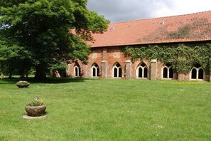 A building with a red-tiled roof and arched windows, surrounded by a well-maintained lawn and a large tree. - Börstel Abbey - Washhouse (Berge)