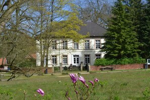 A two-story building with a brick facade, a tiled roof, and a front garden with flowering plants. - Börstel Abbey - Washhouse (Berge)