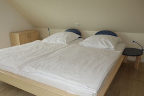 Ein Doppelbett mit weißer Bettwäsche, ein Holz-Kopfteil und ein Nachttisch mit Lampe.