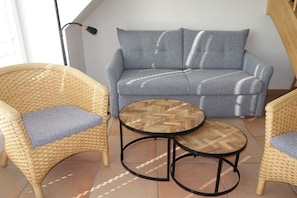 Ein Zimmer mit einem grauen Sofa, zwei Korbstühlen mit Kissen und einem kleinen Holztisch.