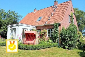 A two-story house with a red-tiled roof, a white exterior, and a garden with a red chair and plants. - Holiday home in Waabs with swimming pool (Waabs)