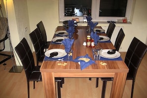 Ein Esstisch ist für sechs Personen gedeckt, mit Tellern, Besteck und blauen Servietten.