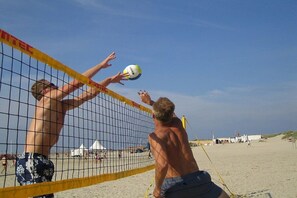 Un match de volleyball de plage où les joueurs tentent d’atteindre le ballon au-dessus du filet.