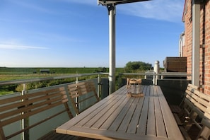 Ein Holztisch und Bänke auf einem Balkon mit Blick auf ein grünes Feld und einen klaren Himmel.