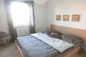Ein Schlafzimmer mit einem Bett, einem Sessel, einem Fenster mit Vorhängen und motivierender Wandkunst.