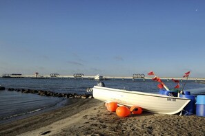 Een boot met het nummer 'DAH 100' op een zandstrand, met een pier op de achtergrond.