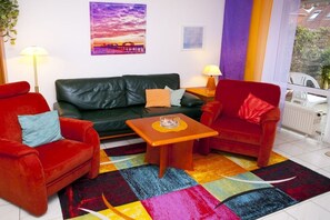 A living room with a black leather sofa, two red armchairs, a small wooden table, and a colorful rug. - Beach shell Kellenhusen (Kellenhusen)