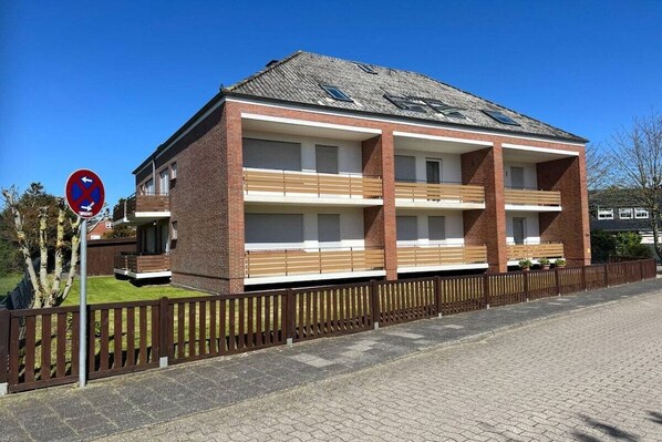 Un immeuble à deux étages avec une façade en briques, de nombreux balcons et une entrée fermée par un portail.