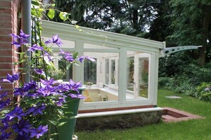 A conservatory with a brick wall and a green planter with purple flowers. - Holiday apartment with 2 bedrooms (Neuenkirchen OT Delmsen)