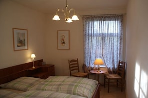 A room with a bed, two chairs, a small table with a lamp, a window with curtains, and two wall-mounted lamps. - Holiday apartment with 2 bedrooms (Neuenkirchen OT Delmsen)