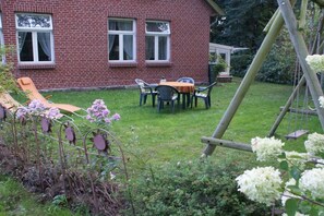 A brick house with a patio area, a swing set, and a table with chairs. - Holiday apartment with 2 bedrooms (Neuenkirchen OT Delmsen)