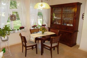 Ein Essbereich mit einem Tisch für vier Personen, umgeben von Stühlen, einer Vitrine und einem Fenster mit Vorhängen.